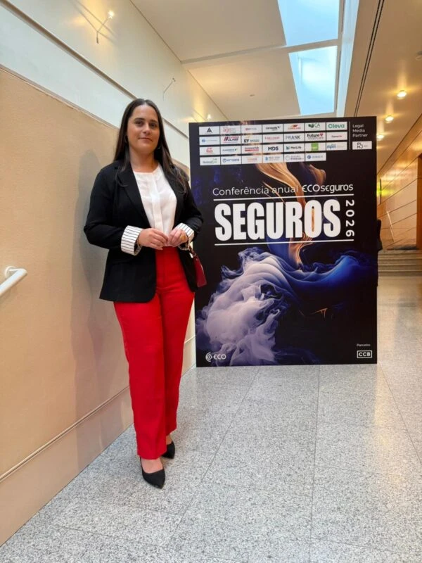 Vânia, colaboradora da EMAX Seguros, junto ao cartaz da Conferência Anual de Seguros 2026 em Lisboa